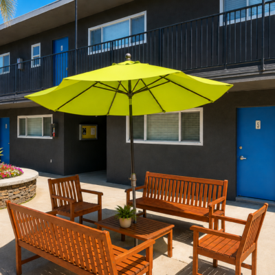 Outdoor communal seating area with lime-green umbrella, wooden benches and table in front of dark apartment building with blue doors.