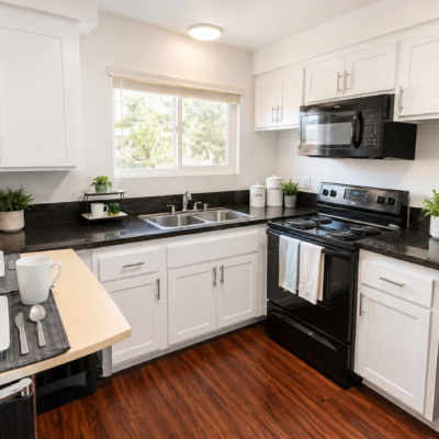 Bright modern kitchen with white cabinets, black granite counters, double sink, and black appliances; dining table set with dishes.